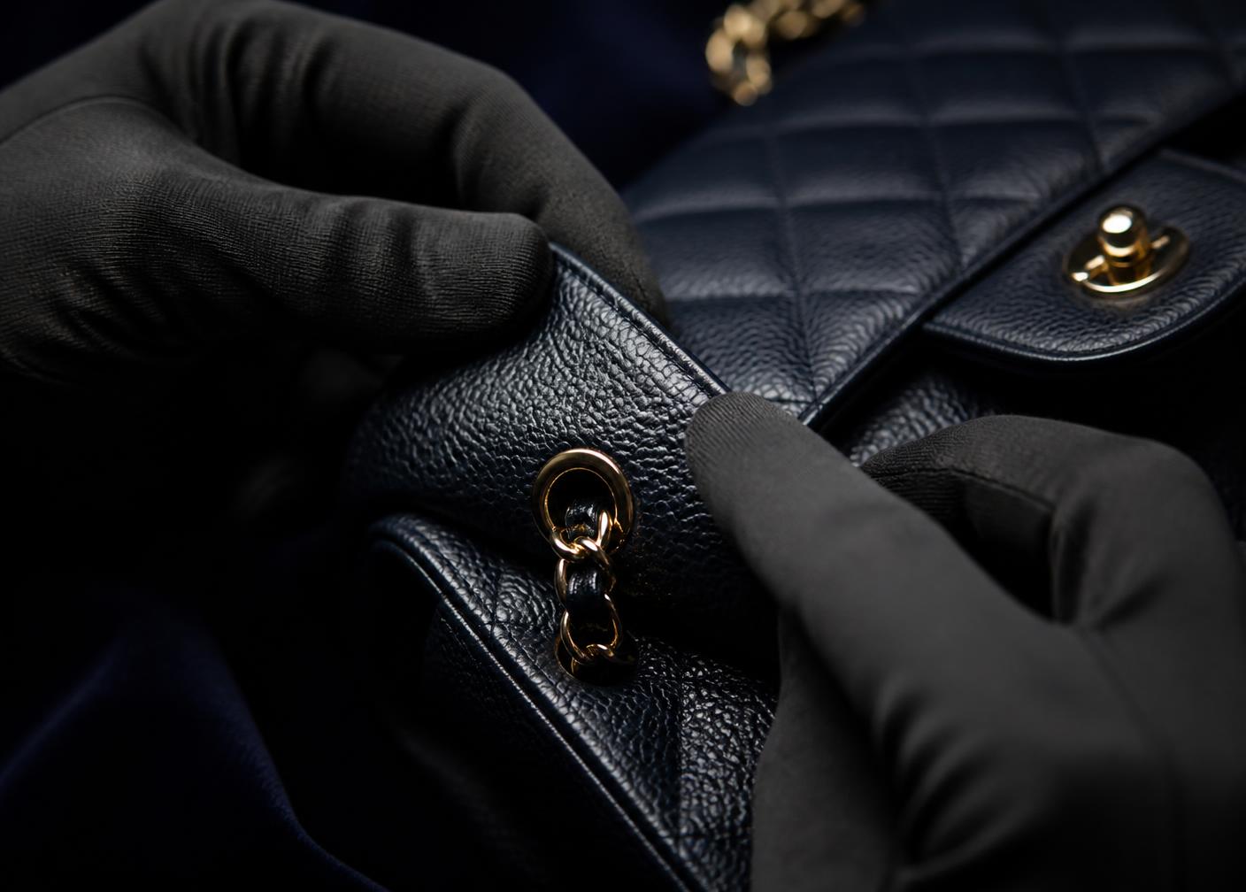 Een zwarte gewatteerde leren handtas die met zwarte handschoenen gedetailleerd wordt onderzocht