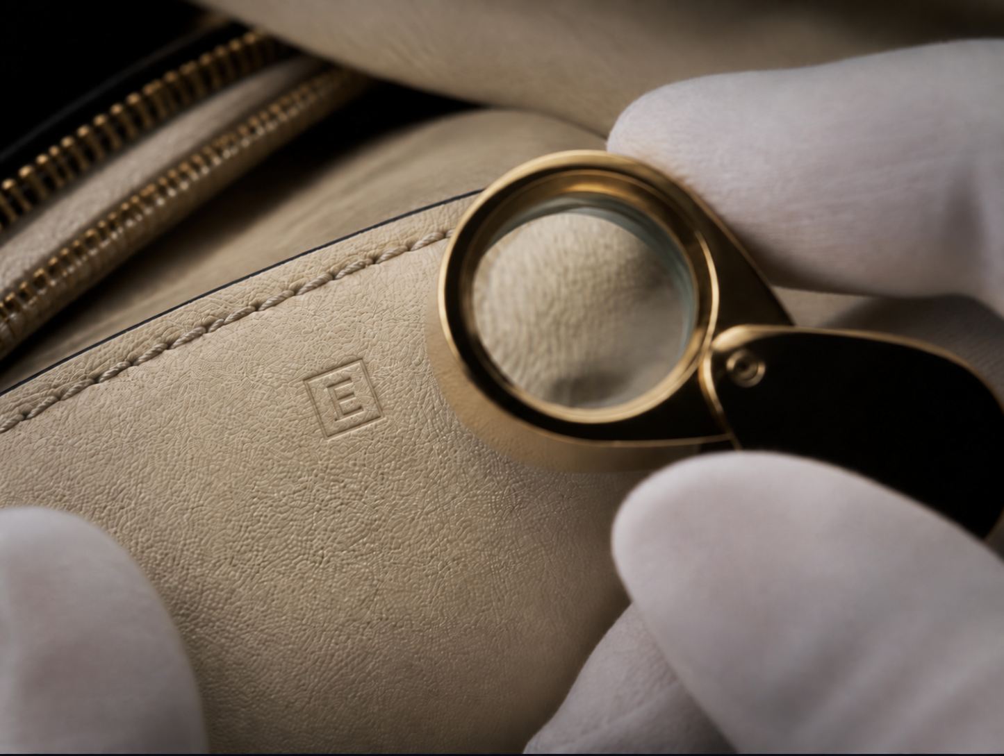 Close-up van crèmekleurig leer, stiksels en een loep tijdens een gedetailleerd onderzoek van luxe mode.